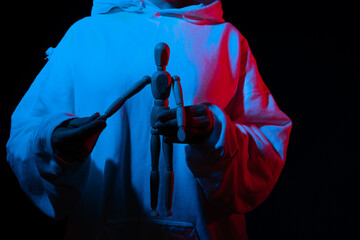 Person in hoodie presenting a wooden mannequin under colored lighting