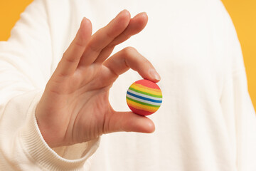 A hand presenting a colorful striped ball against yellow