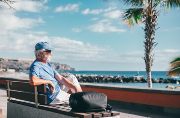 Senior bearded man sitting outdoors on bench face the sea enjoying sunny day, travel, vacation,...