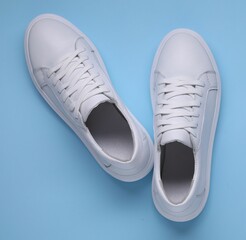 Pair of stylish white sneakers on light blue background, top view