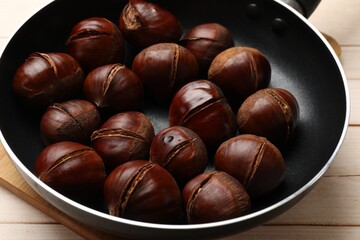 Roasted edible sweet chestnuts in frying pan on wooden table, closeup