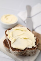 Slices of tasty bread with butter on white tiled table, closeup. Space for text