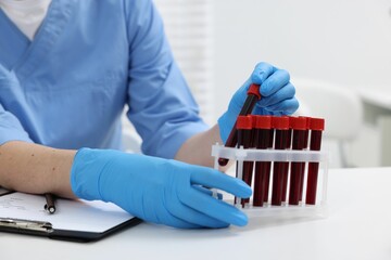 Laboratory testing. Doctor with blood samples in tubes at white table indoors, closeup