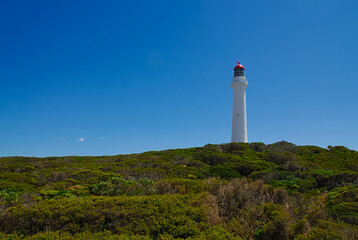 Fototapeta na wymiar A tall white and red lighthouse stands proudly against a clear blue sky on a beautiful sunny day.