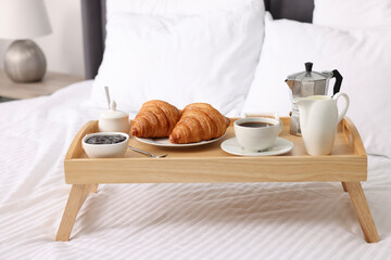 Wooden tray with tasty breakfast on bed at home