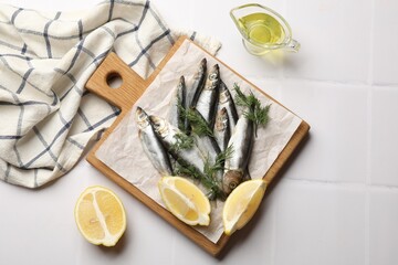 Fresh raw sprats, dill, oil and cut lemon on white tiled table, flat lay