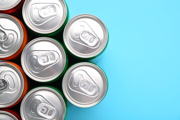 Energy drink in cans on light blue background, top view. Space for text