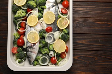 Raw fish with vegetables and lemon in baking dish on wooden table, top view. Space for text