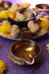 Diwali celebration. Diya lamp on shiny violet table, closeup