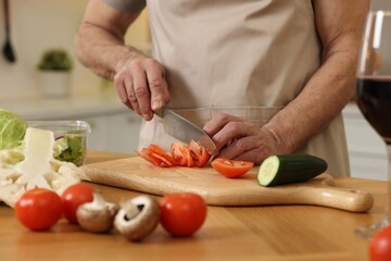 Obraz na płótnie Canvas Man cutting tomato at wooden table in kitchen, closeup