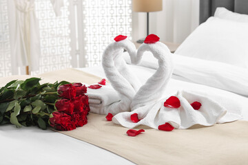 Obraz na płótnie Canvas Honeymoon. Swans made of towels and beautiful red roses on bed in room