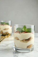 Delicious tiramisu in glass and mint leaves on white marble table
