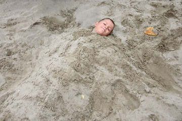 Young boy buried up to his neck in sand.