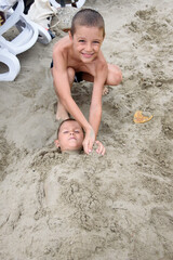 Young boy buried up to his neck in sand.