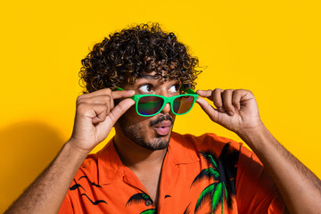 Photo of astonished man dressed print shirt holding sunglass staring at impressive offer empty space isolated on yellow color background