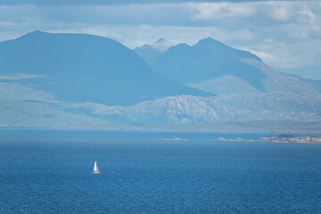 Sailboat glides on blue ocean water along scenic hilly coast of Scottish islands