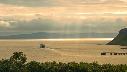 Sun shines through clouds and reflects off sea as ferry sails on regular route