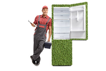 Repairman with a clipboard and a tool box leaning against a green sustainable fridge