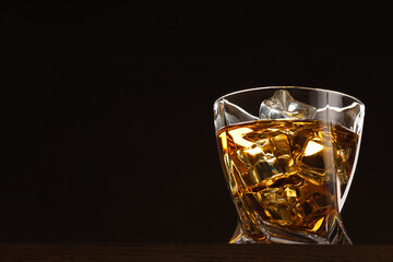 Whiskey with ice cubes in glass on table against black background. Space for text