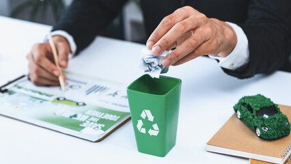 Businessman put paper waste on small tiny recycle bin in his office symbolize corporate effort on...