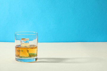 Whiskey with ice cubes in glass on white table against light blue background, space for text
