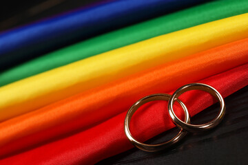 Rainbow LGBT flag and wedding rings on black wooden background