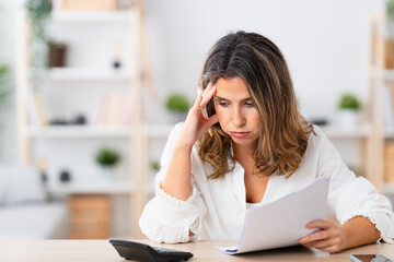 Woman looking stressed out while using calculator to calculate home finances