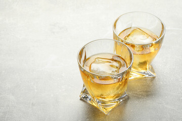 Tasty whiskey with ice in glasses on light table, closeup. Space for text