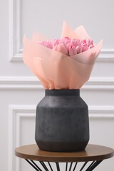 Bouquet of beautiful pink tulips in vase on wooden table near white wall
