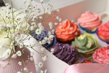 Different colorful cupcakes in box and flowers on table, closeup
