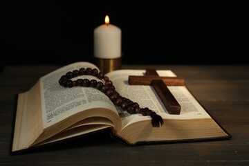 Church candle, Bible, rosary beads and cross on wooden table, closeup