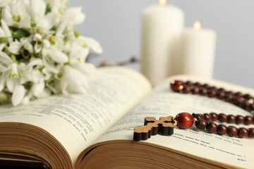 Bible, rosary beads, flowers and church candles on table, closeup