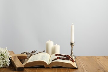 Church candles, cross, rosary beads, Bible and willow branches on wooden table against light...