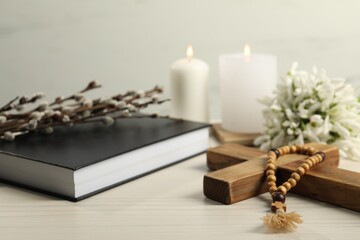 Wooden cross, rosary beads, Bible, church candles and snowdrops on white table