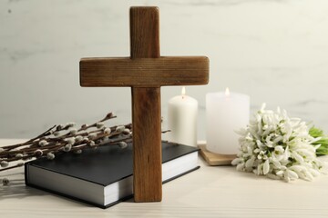 Wooden cross, Bible, church candles, willow branches and snowdrops on white table