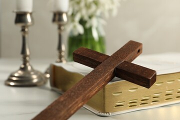 Wooden cross and Bible on white table, closeup