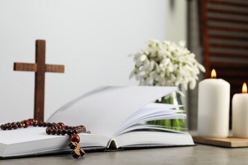 Church candles, Bible, wooden cross, rosary beads and flowers on grey table