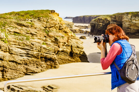 Woman with camera at Cathedral Beach in Spain.