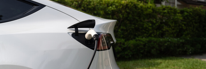 Fototapeta na wymiar Closeup EV charger plug handle attached to electric vehicle port, recharging battery from charging station. Modern designed EV car and clean energy sustainability for better future.Panorama Synchronos