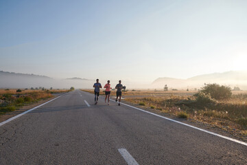 Obraz premium A group of friends, athletes, and joggers embrace the early morning hours as they run through the misty dawn, energized by the rising sun and surrounded by the tranquil beauty of nature