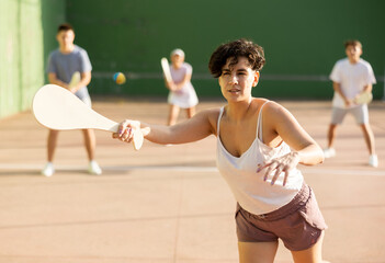 Fototapeta premium Latin woman serving ball with paleta during Basque pelota game outdoors. Woman playing pelota on outdoor fronton.