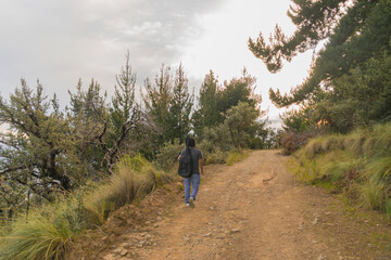 man hiking in mountain carrying a guitar towards the horizon with the sunset sun