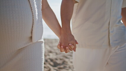 Pregnant couple holding hands walking beach closeup. Expecting pair strolling