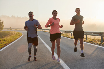 A group of friends, athletes, and joggers embrace the early morning hours as they run through the misty dawn, energized by the rising sun and surrounded by the tranquil beauty of nature