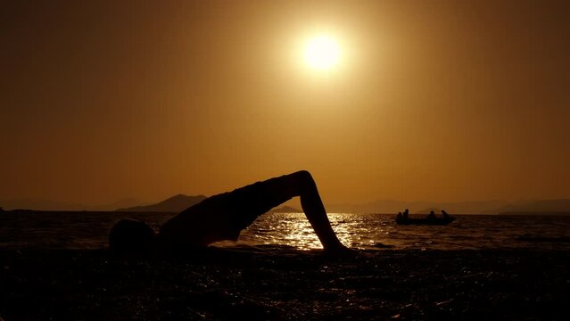 Silhouette of girl perform stretch. A calm girl resting in yoga pose on the beach during nightfall time. A concept of sporty teenagers life and healthy lifestyle.