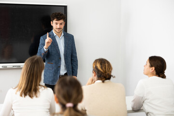 Fototapeta premium Positive male trainer, conducting advanced training courses to office employees sitting at desks in auditory