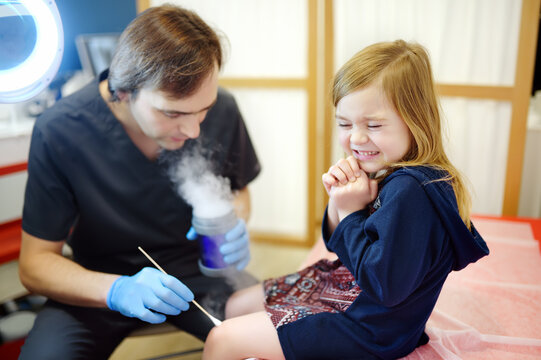 A caring doctor checks moles on the skin of a small child. Dermatologist remove of benign tumors with liquid nitrogen for cute preschooler girl. Baby fears of treat.