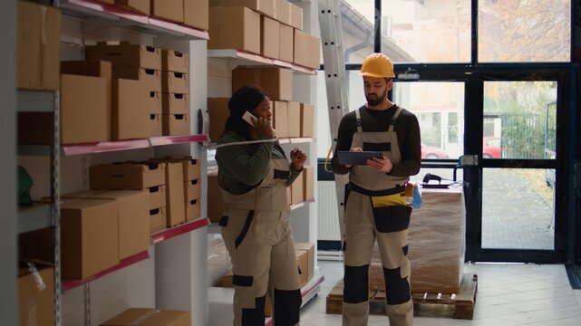 Chief logistics officer and employee preparing warehouse orders for delivery, using tablet to verify shipping informations, receiving phone call while scanning parcels labels in repository