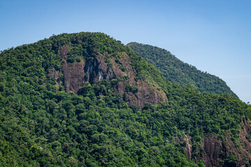 Fototapeta premium Rock formations covered by dense Atlantic Forest green vegetation viewed from Mirante do Cristo observation deck under summer afternoon sunny clear blue sky near Petropolis, Rio de Janeiro - Brazil.