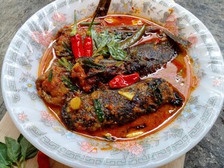 Mangut lele placed in a plate isolated on cement floor background. Dish made from fried catfish, chili, basil, coconut milk and some spices. Yogyakarta traditional dish. Indonesian food.
